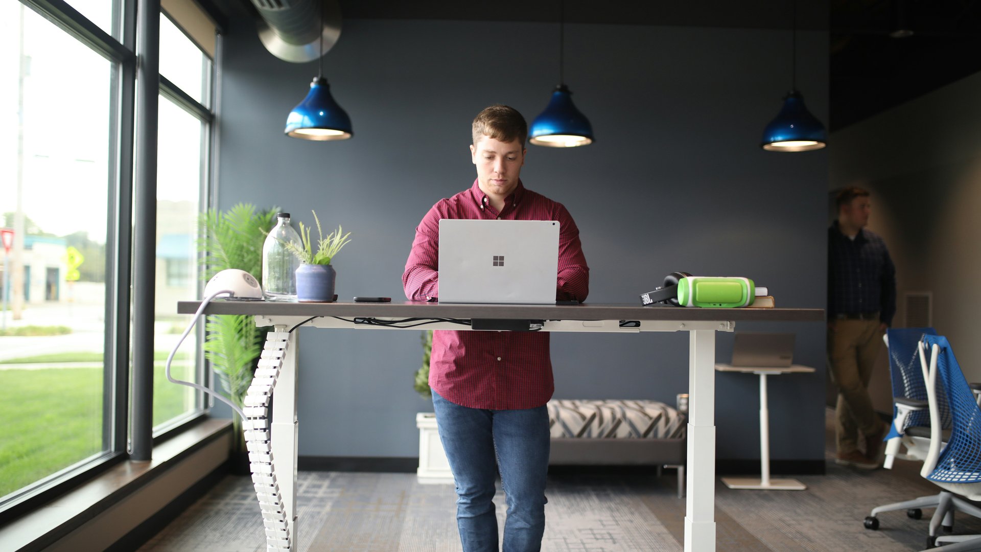 A man standing at his standing desk working on his laptop in a modern workspace.
